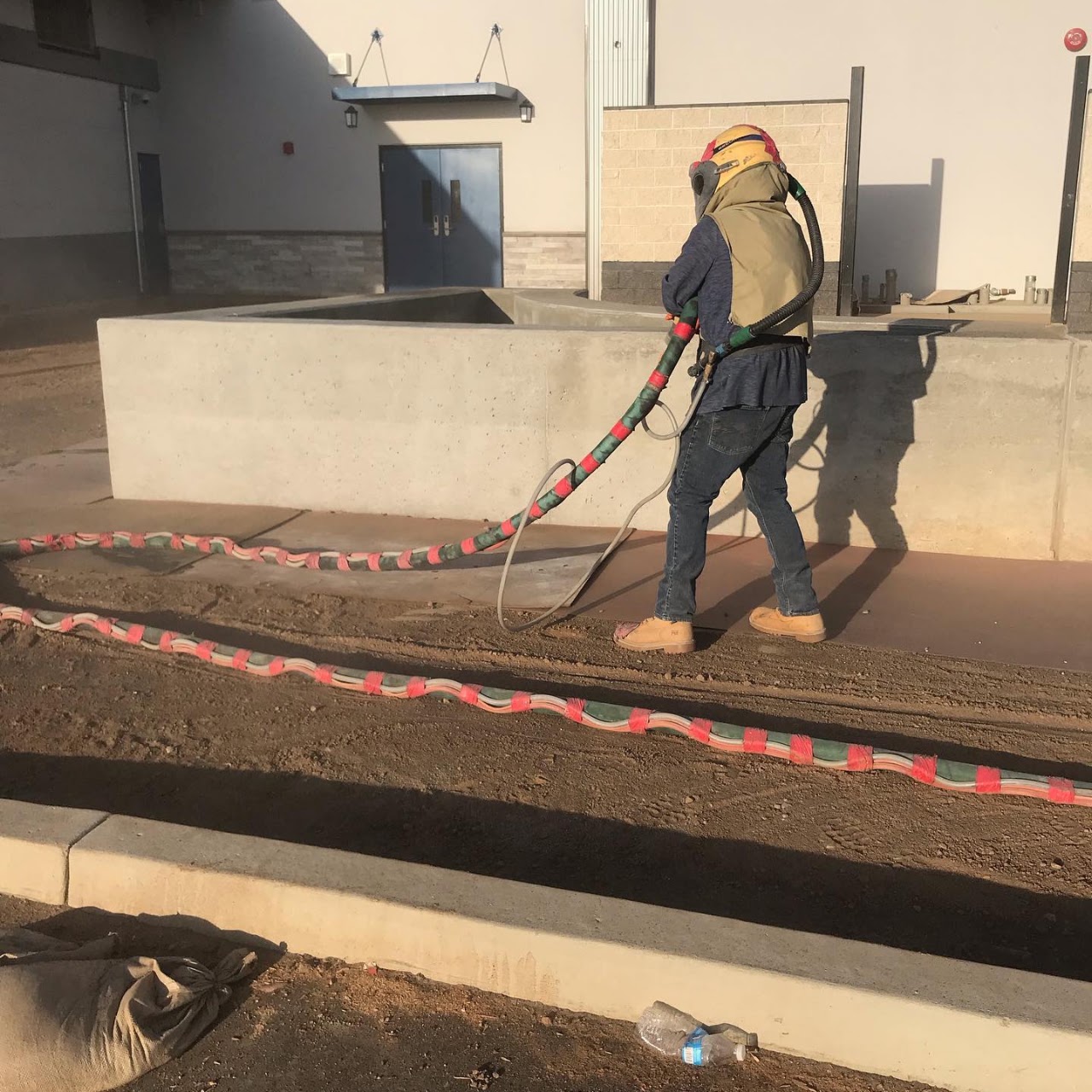 A sandblasting operator in protective gear blasting a concrete slab outside a commercial building