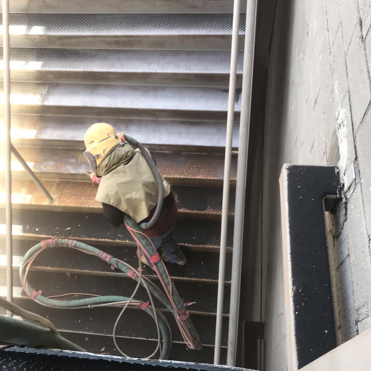 A sandblasting operator in a protective hood working on an exterior concrete stairway